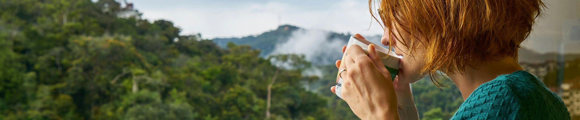 A woman enjoys morning coffee while gazing at a scenic mountain view.