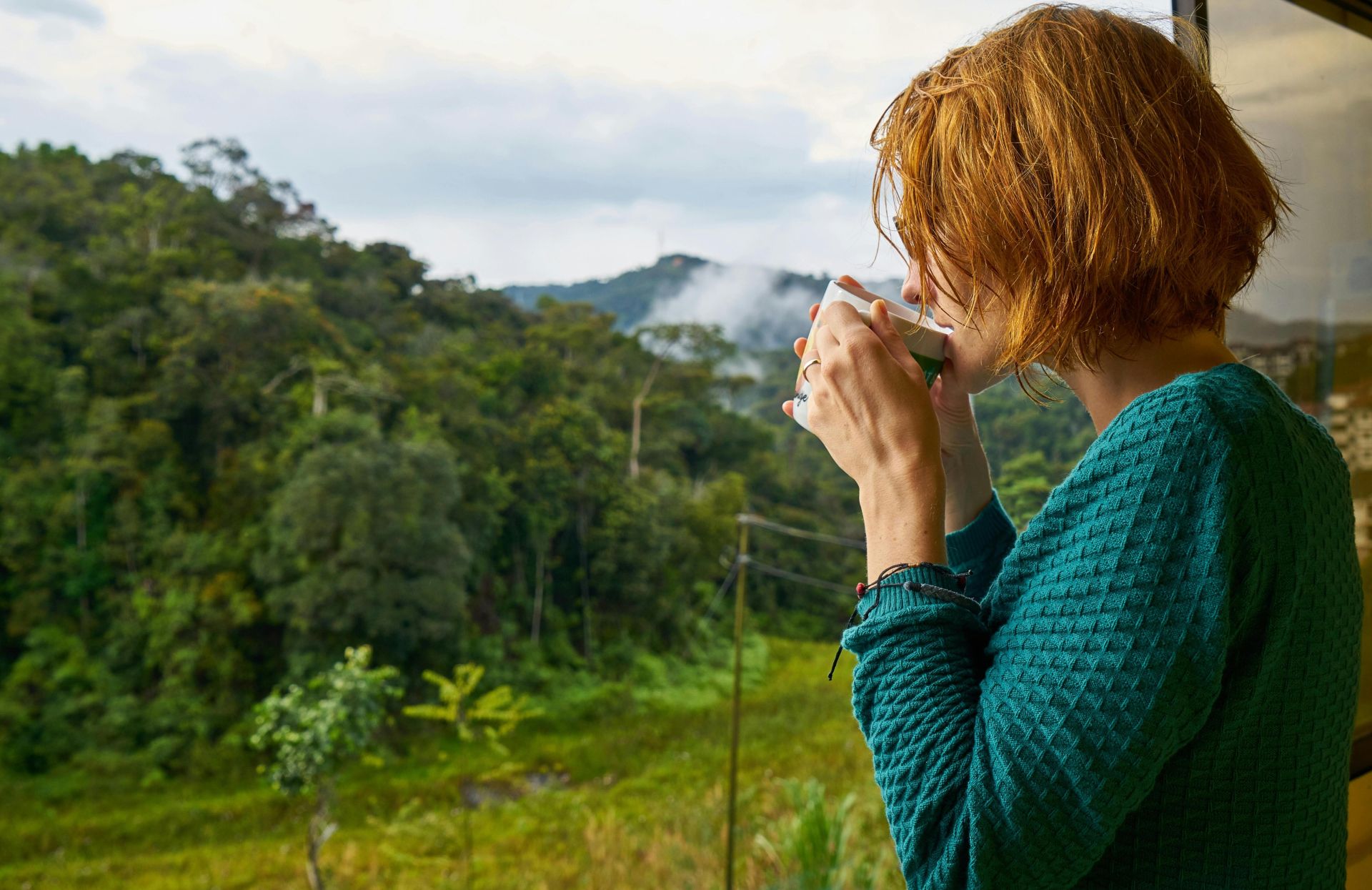 A woman enjoys morning coffee while gazing at a scenic mountain view.