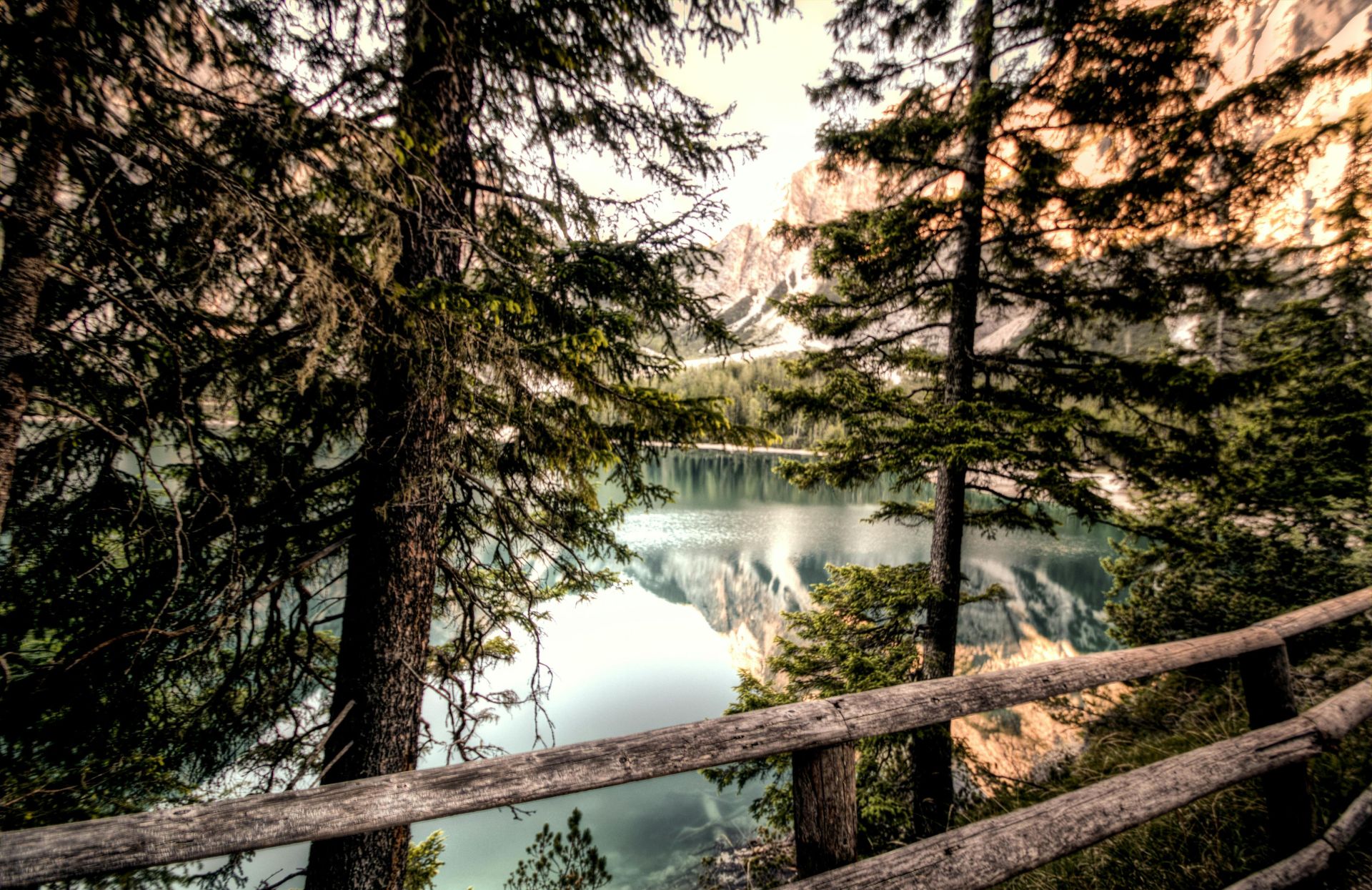 Captivating view of a tranquil mountain lake framed by trees and a rustic fence.