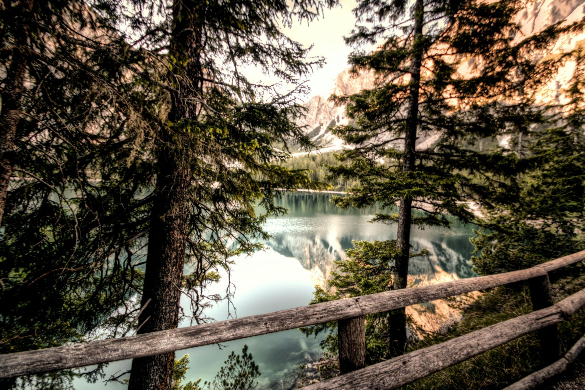 Captivating view of a tranquil mountain lake framed by trees and a rustic fence.