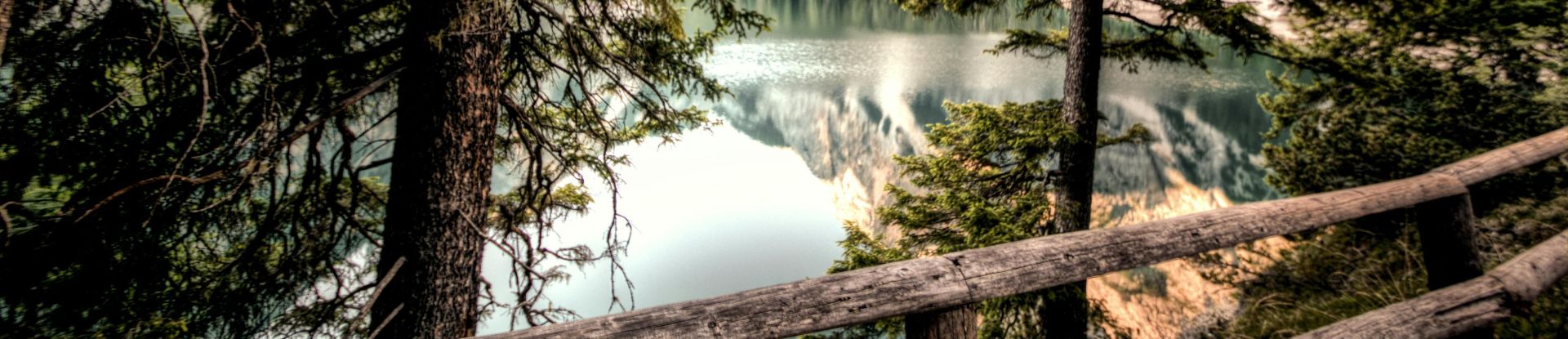 Captivating view of a tranquil mountain lake framed by trees and a rustic fence.
