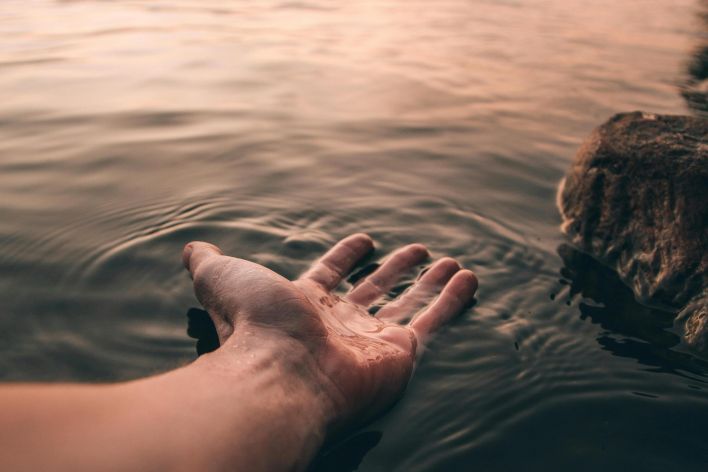 A serene image of a hand touching the water at twilight, creating gentle ripples.