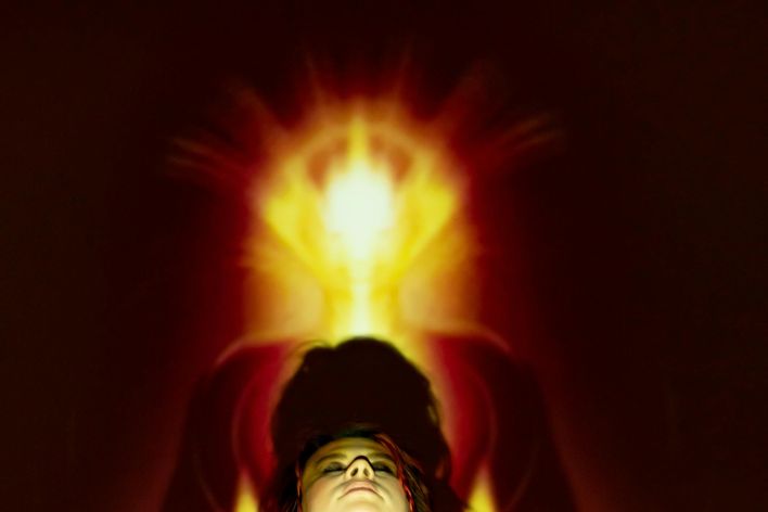 A woman meditates with a vibrant aura and light projections creating a spiritual ambience.